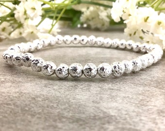 May include: A silver lava rock beaded bracelet. The beads are small and round, with a textured surface.