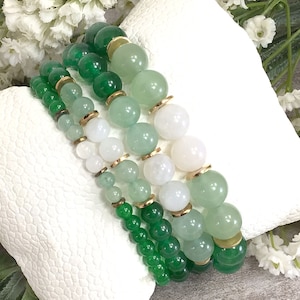 May include: A set of four bracelets featuring green and white gemstone beads with gold accents. The bracelets are stacked on top of each other, creating a layered look.
