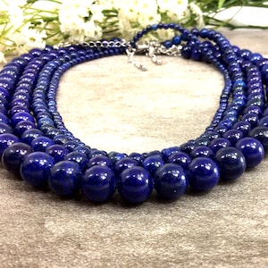 May include: A multi-strand necklace made of dark blue lapis lazuli beads. The necklace is made of five strands of beads, each with a different size bead. The beads are round and have a smooth, polished finish.
