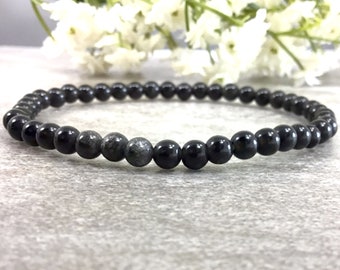May include: A black beaded bracelet with a single grey bead. The bracelet is made of small, round beads and is approximately 7 inches in length.