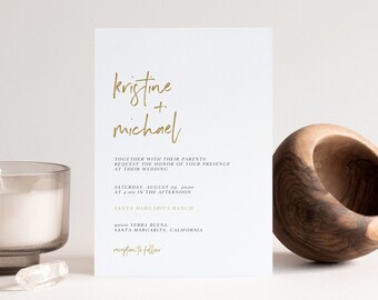 Puede incluir: Una invitación de boda blanca con caligrafía dorada que dice "kristine + michael" y detalles sobre la ceremonia y la recepción de la boda. La invitación está sobre una superficie blanca con un cuenco de madera y una vela.