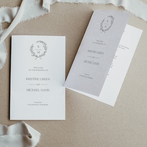 May include: A wedding invitation with a simple design featuring a wreath with the initials "K" and "M" and the text "Welcome to the wedding of Kristine Green and Michael Davis" with the date and location of the wedding.