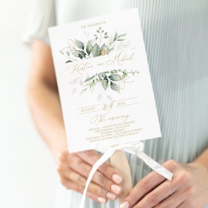 May include: A white wedding program fan with green and gold floral designs. The text reads "The Wedding of Kristine and Michael August 24th, 2023 The Ceremony" followed by a list of ceremony events.