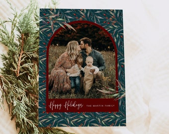 Peut inclure: Une carte de Noël représentant une famille de quatre personnes dans un champ vert. Les parents s'embrassent et les deux enfants se tiennent devant eux. La carte a un fond bleu foncé avec une bordure rouge et un motif de feuilles et de baies. Le texte "Joyeuses Fêtes" et "La famille Martin" est imprimé en rouge en bas de la carte.