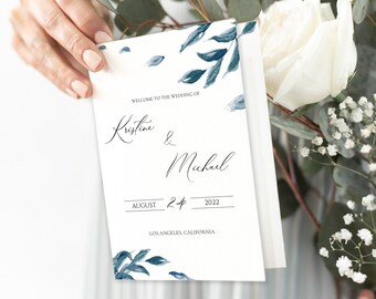 May include: A white wedding invitation with blue watercolor leaves and the text "Welcome to the wedding of Kristine & Michael August 24, 2022 Los Angeles, California"