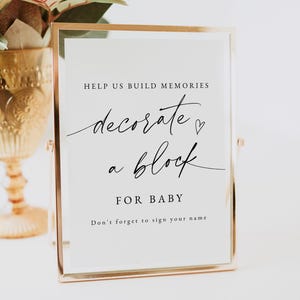 以下が含まれることがあります： 「HELP US BUILD MEMORIES decorate a block FOR BABY Don't forget to sign your name」というテキストが書かれた、金色のフレームに入った白い看板です。