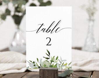 May include: White card with black calligraphy that says "table 2" and a green watercolor floral design at the bottom.