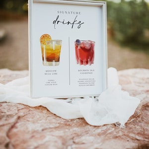 May include: A white sign with the word "SIGNATURE drinks" written in black cursive. The sign features two illustrated cocktails, a Moscow Mule Lime and a Bourbon Old Fashioned, with their ingredients listed below.