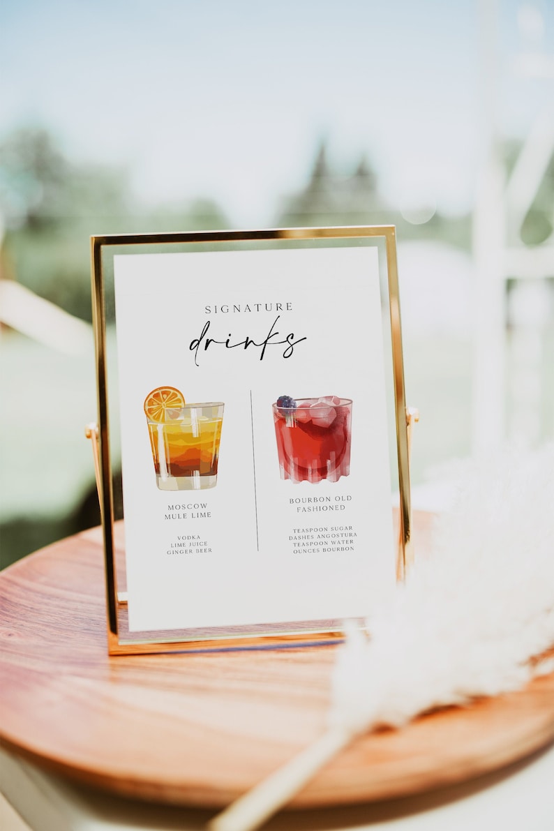 May include: A gold framed sign with the text "SIGNATURE drinks" at the top. The sign lists two cocktails, a Moscow Mule Lime and a Bourbon Old Fashioned, with illustrations of each drink and their ingredients.