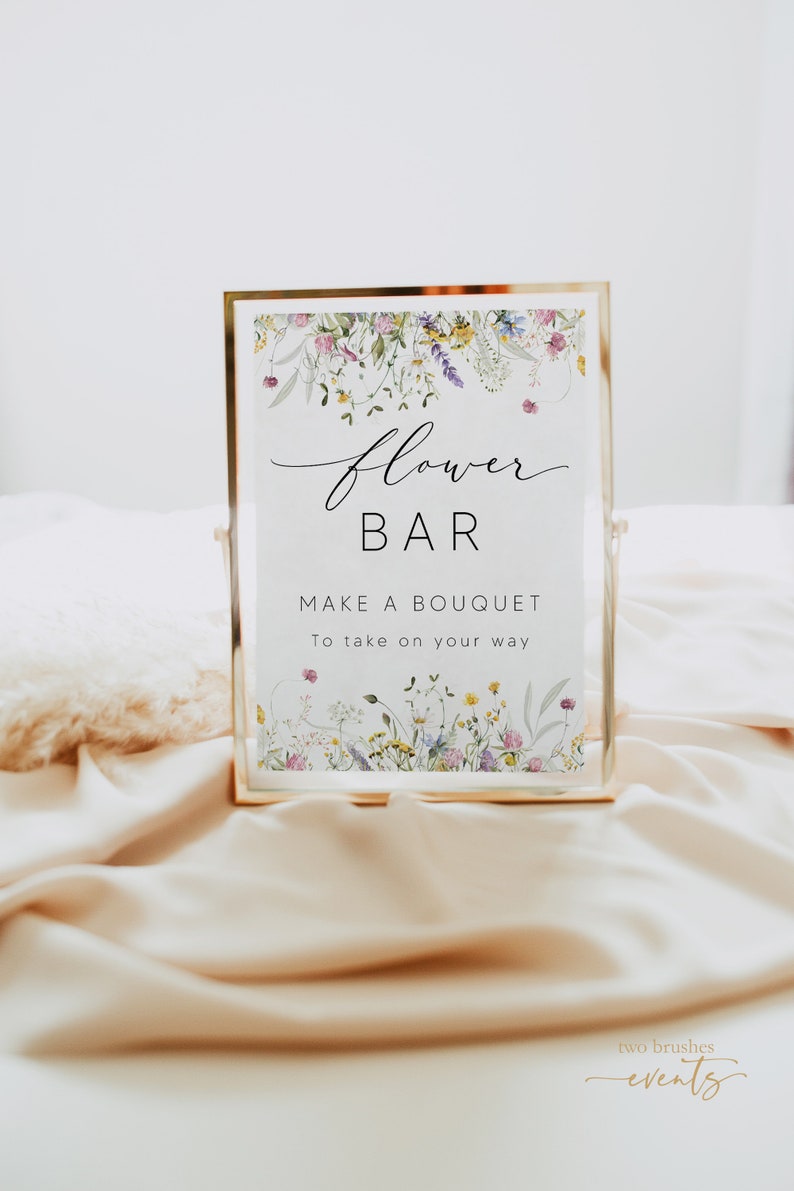 Pu&ograve; includere: Un cartello con cornice dorata con le parole "Flower Bar" in elegante scrittura, che invita gli ospiti a "Make a Bouquet". Il cartello &egrave; adornato da un bordo floreale di fiori selvatici e poggia su una superficie satinata.