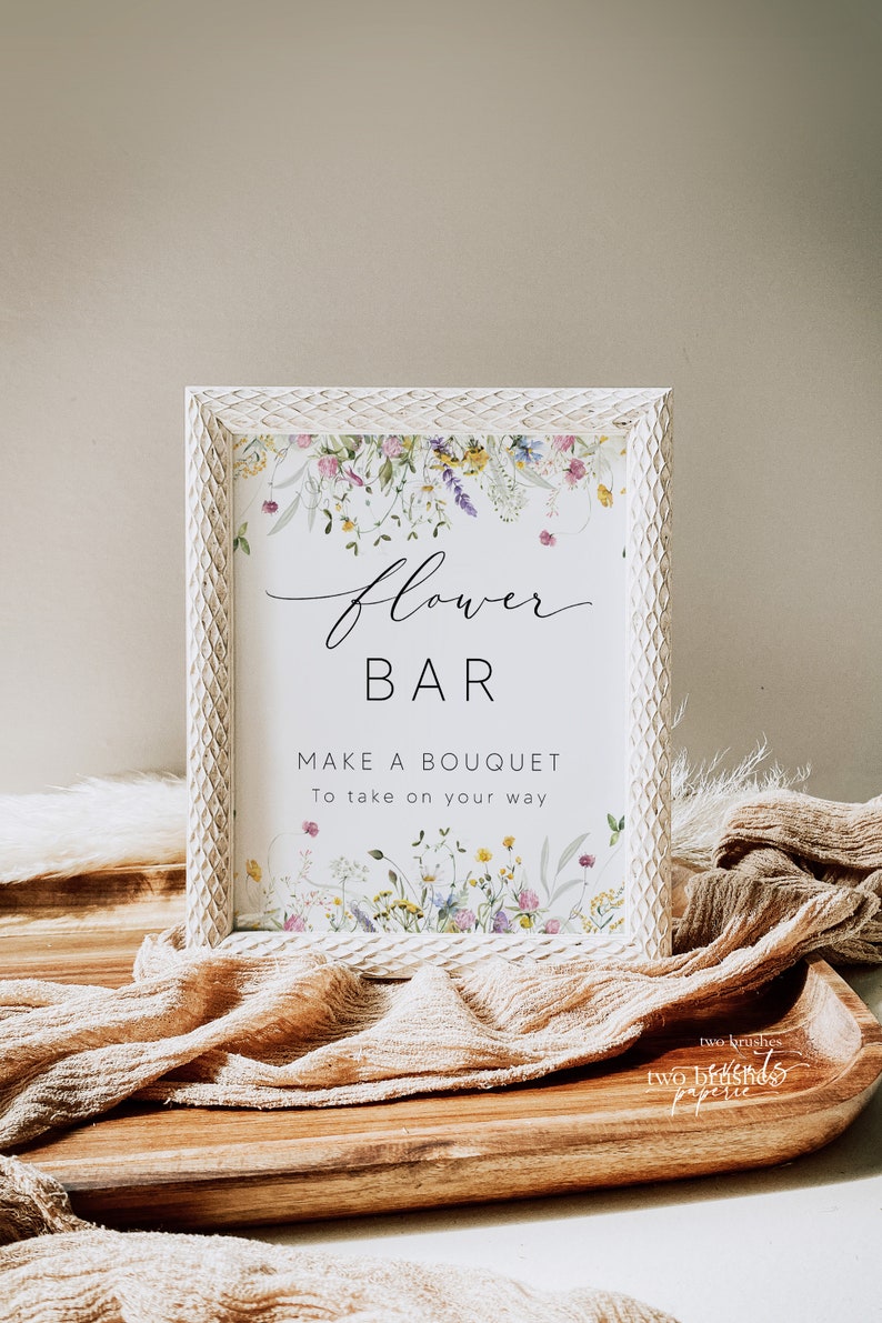 Pu&ograve; includere: Un cartello incorniciato con le parole "Flower Bar" e "Make a Bouquet" in elegante scrittura. Il cartello &egrave; decorato con illustrazioni floreali ad acquerello e posto su un vassoio di legno con un tessuto strutturato.