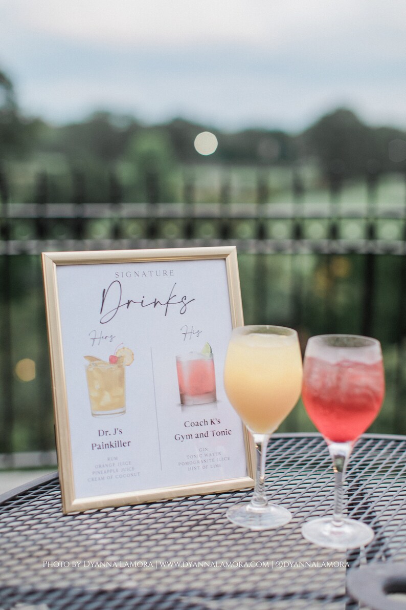 May include: A framed sign with the title "Signature Drinks" lists two cocktails: "Dr. J's Painkiller" and "Coach K's Gym and Tonic". The sign is next to two glasses of cocktails, one yellow and one pink.