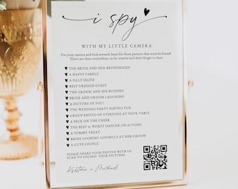 May include: A framed wedding game card with the words "i spy" at the top. The card includes a list of photo prompts and instructions. The frame is gold-colored, and the text is in black.