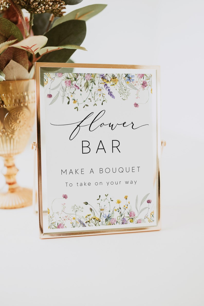 Pu&ograve; includere: Un cartello rettangolare in una cornice dorata con le parole "flower BAR" in corsivo nero. Il cartello recita anche "MAKE A BOUQUET To take on your way." Illustrazioni floreali bordano la parte superiore e inferiore del cartello.