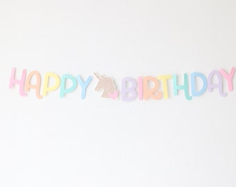 May include: A pastel rainbow colored banner with the words "Happy Birthday" and a glitter unicorn head in the middle.