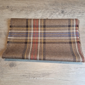 May include: Folded brown plaid fabric with red, blue, and yellow stripes. The fabric has a fringed edge and is displayed on a wooden surface. The text "Art et Mode Creations" is visible at the bottom.