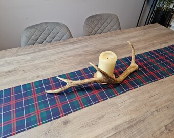 May include: A blue, green, and red plaid table runner with a white antler centerpiece and a white candle on a wooden table.