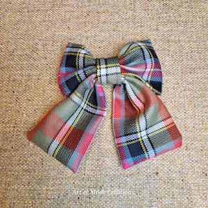 May include: A hair bow featuring a multi-colored plaid pattern with shades of green, red, blue, yellow, and black. The bow has two long, angled tails and a central knot. The text Art et Mode Creations is printed at the bottom.
