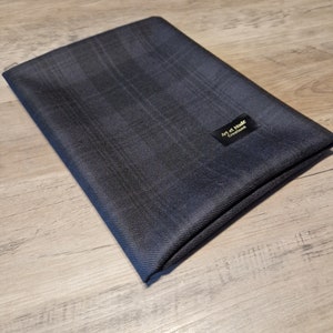 May include: A folded, dark blue fabric with a plaid pattern. A small black label with gold text reads "Art et Mode Creations". The fabric is lying on a light wood surface.
