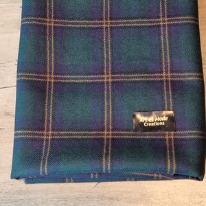 May include: A folded green, blue, and gold plaid fabric with a black label that reads "Art et Mode Creations".