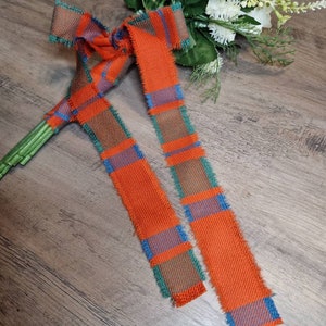 May include: Two orange and green tartan ribbons with frayed edges. The ribbons are tied together in a bow.