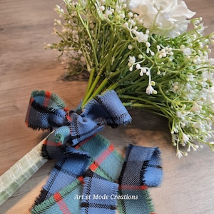 May include: A wedding bouquet with white flowers and foliage, adorned with a blue, green, and red tartan ribbon. The handle is wrapped in a pale green satin ribbon. The text "Art et Mode Creations" is visible.