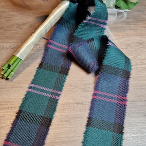 Könnte beinhalten: Ein grünes, blaues und pinkfarbenes Tartanband mit ausgefransten Kanten. Das Band ist zu einer Schleife gebunden und wird verwendet, um einen Blumenstrauß zu dekorieren.