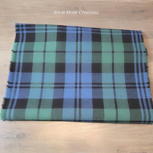 以下が含まれることがあります： 青、緑、黒の色合いのチェック柄の、折りたたまれた長方形のスカーフ。 スカーフにはフリンジエッジがあります。 テキスト「Art et Mode Creations」は左上にあります。