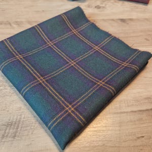 以下が含まれることがあります： チェック柄の正方形の布。生地は、ティール、ネイビーブルー、パープル、ゴールドの色使いです。チェック柄は、交差する線で構成され、グリッドのようなパターンを作成します。生地は、衣類や室内装飾に使用される可能性があります。