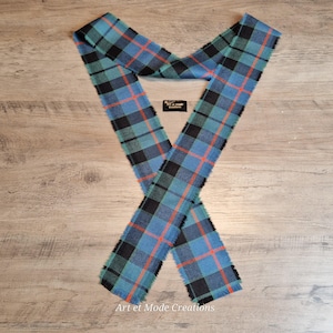 May include: A blue, black, and orange plaid scarf with fringed edges. The scarf is made of a soft fabric and is laid out in an X shape. The scarf has a teal and black plaid pattern with orange lines. The scarf is labeled "Art et Mode Creations."