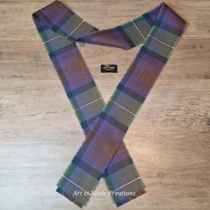 May include: A plaid scarf in shades of purple, green, and brown, with a fringed edge. The scarf is laid out on a wooden surface. The text "Art et Mode Creations" is visible.