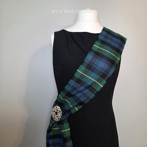 May include: A black dress with a blue, green, and yellow tartan sash. A silver brooch fastens the sash. The text "Art et Mode Creations" is in the upper left corner.
