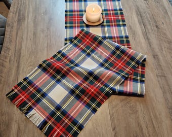 May include: A red, green, blue, and yellow plaid table runner and matching placemat. A lit candle sits on a wooden coaster on the runner. The placemat has fringed edges. The text "Art et Mode Creations" is visible.