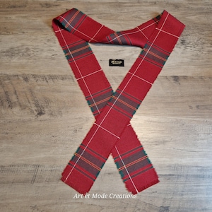 May include: A red plaid scarf with green, white, and yellow accents. The scarf is made of a woven fabric and has a fringed edge. The text "Art et Mode Creations" is visible.