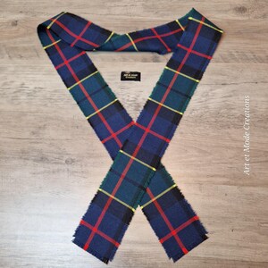 Op de afbeelding: Een blauw, groen en rood geruite sjaal met gele accenten. De sjaal is gemaakt van een zachte stof en heeft een gefranjerde rand. De sjaal ligt op een houten oppervlak en is ongeveer 150 cm lang.