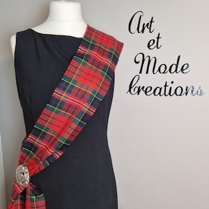 May include: A black dress is styled with a red, green, and blue tartan sash, fastened with a silver brooch. The image includes the text "Art et Mode Creations" in cursive script.