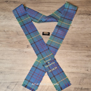May include: A blue, green, and red tartan sash with the names "Connor & Samantha" and the date "06.06.26" embroidered on it. The sash is made of woven fabric and has the text "Art et Mode Creations" at the bottom.