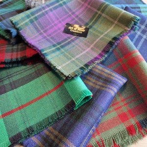 May include: A stack of four different tartan fabrics with fringed edges. The top fabric is a purple, green, and blue tartan with a label that reads "Art et Mode Creations".