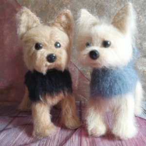 Pode incluir: Duas pequenas figuras de cão Yorkshire Terrier de pelúcia de feltro. O cão à esquerda está vestindo um suéter preto e o cão à direita está vestindo um suéter azul.