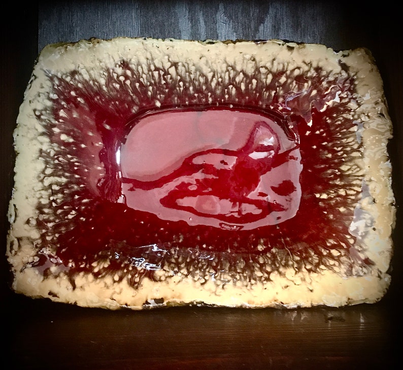 Może przedstawiać: Prostokątne ceramiczne naczynie z czerwoną glazurą i fakturowanym, beżowym brzegiem. Glazura ma błyszczące wykończenie i tworzy unikalny, abstrakcyjny wz&oacute;r.