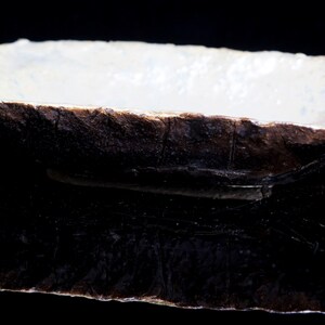 Może przedstawiać: Prostokątne ceramiczne naczynie z białym wnętrzem i ciemnobrązowym zewnętrzem. Naczynie ma szorstką, fakturowaną powierzchnię i wydaje się być wykonane ręcznie.