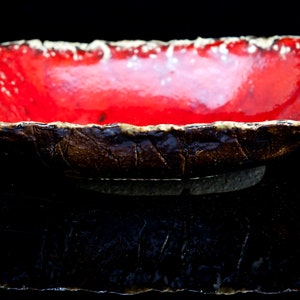 Może przedstawiać: Czerwona ceramiczna miska z fakturowanym brązowym brzegiem. Miska jest szkliwiona i ma błyszczące wykończenie.