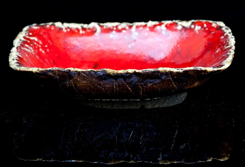 Może przedstawiać: Czerwona ceramiczna miska z fakturowanym brązowym brzegiem. Miska jest szkliwiona i ma błyszczące wykończenie.