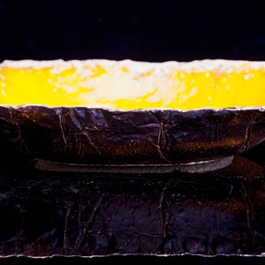 Może przedstawiać: Ż&oacute;łta ceramiczna miska z fakturowanym brązowym zewnętrzem. Miska stoi na czarnej powierzchni.