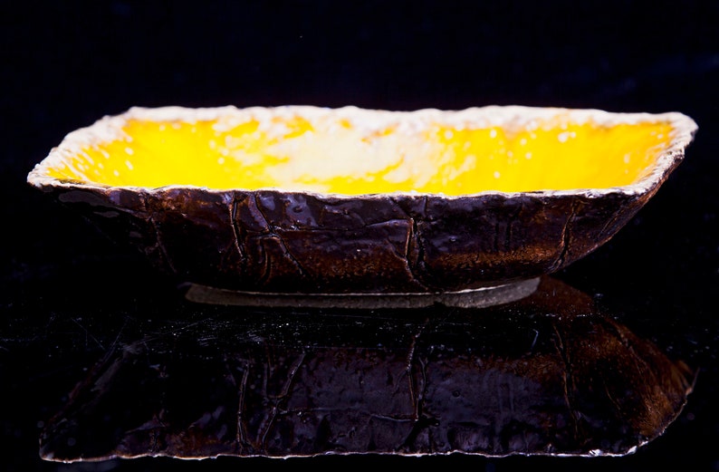 Może przedstawiać: Ż&oacute;łta ceramiczna miska z fakturowanym brązowym zewnętrzem. Miska stoi na czarnej powierzchni.