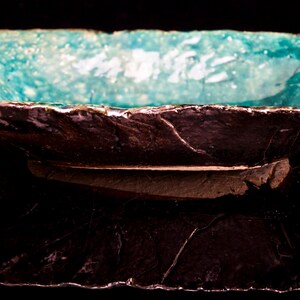 Może przedstawiać: Ceramiczna misa do serwowania w kolorze turkusowym z szorstkim, ciemnobrązowym zewnętrzem. Misa ma nieregularny kształt i lekko uniesiony brzeg.