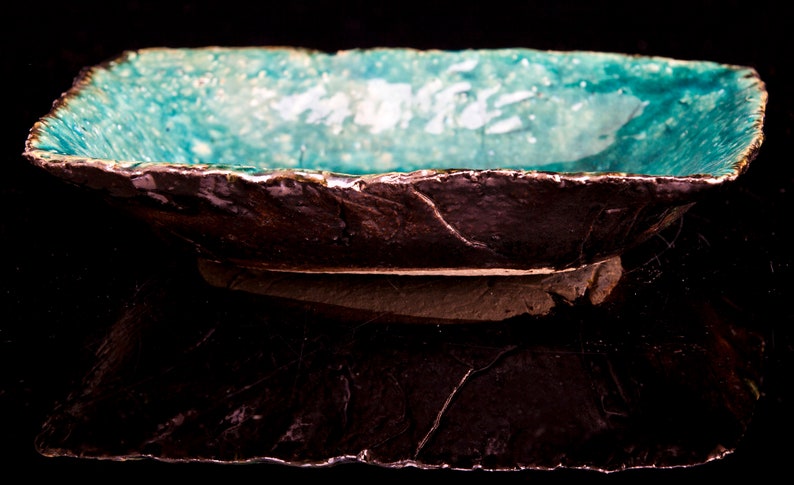 Może przedstawiać: Ceramiczna misa do serwowania w kolorze turkusowym z szorstkim, ciemnobrązowym zewnętrzem. Misa ma nieregularny kształt i lekko uniesiony brzeg.