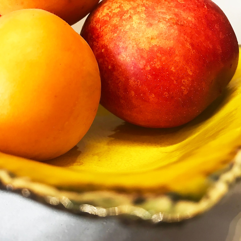 Może przedstawiać: Trzy owoce w ż&oacute;łtej misce. Brzoskwinia czerwona, morela ż&oacute;łta i druga morela ż&oacute;łta.