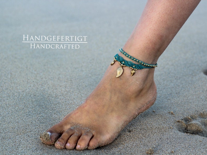 May include: A teal blue and gold ankle bracelet with leaf charms. The bracelet is handmade and the text "HANDGEFERTIGT HANDCRAFTED" is visible in the image.