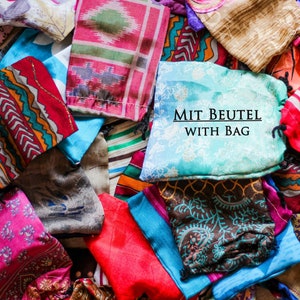 May include: A pile of colorful fabric squares with various patterns. The fabric squares are arranged in a random order. The text "MIT BEUTEL WITH BAG" is printed on a light blue fabric square.